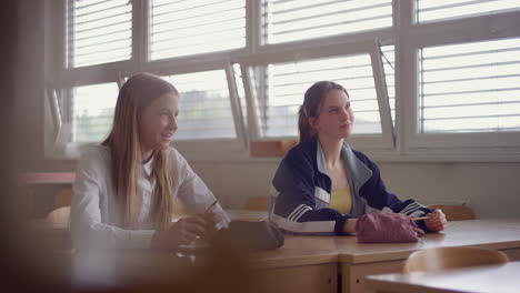 Two-teenage-schoolgirls-sitting-at-a-school-desk-in-the-classroom,-handheld-shot