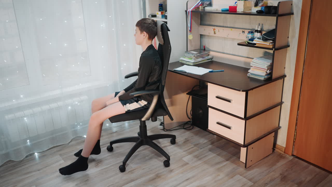 White grandson spinning office chair by window pausing study to daydream, socks on feet, sunlight through curtain, gentle giggles and yawns, shifting posture and restless mood, short break