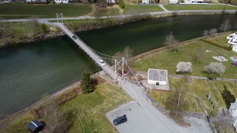 Two-cars-crossing-over-Modalen-river-on-old-suspension-bridge---Aerial-Modalen-Norway-with-church