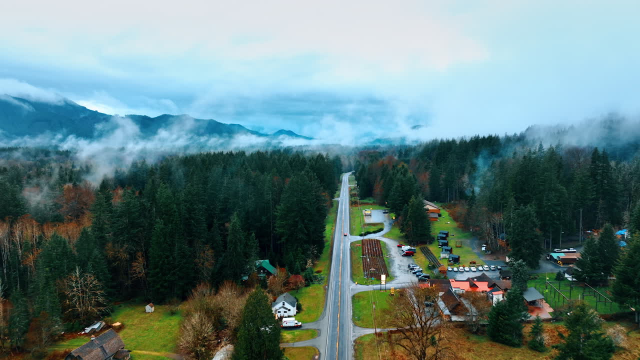 Following the car riding by the straight highway across the Mount Rainier National Park in Washington State, the USA. Top view on some recreational area with cottages around the road. Thin mist rises in the air.