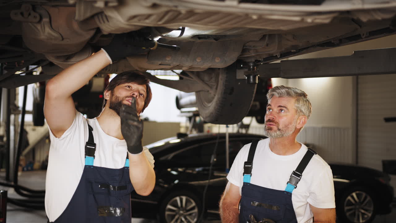 dos mecánicos inspeccionando el tren de aterrizaje del coche