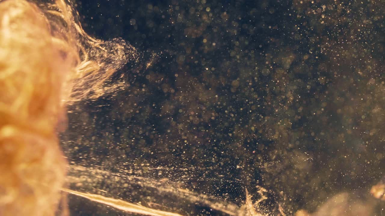 황금 잉크 입자는 검은 바탕에 다채로운 혼란으로 물에 흐른다.