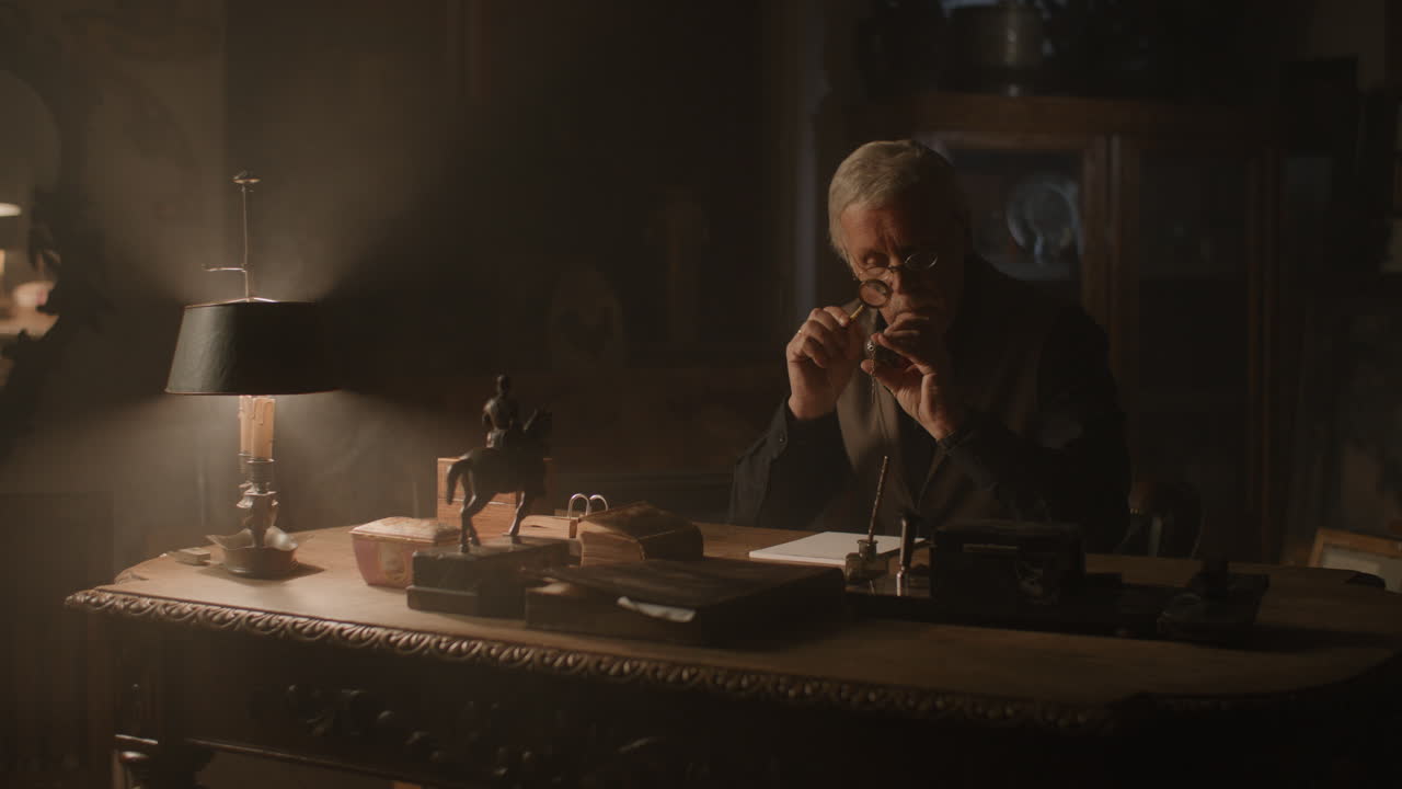 Older passionate man evaluates an old silver skull watch in his office at night