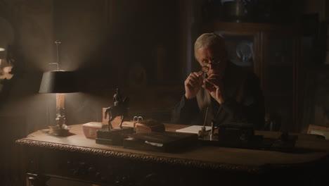 older passionate man evaluates an old silver skull watch in his office at night