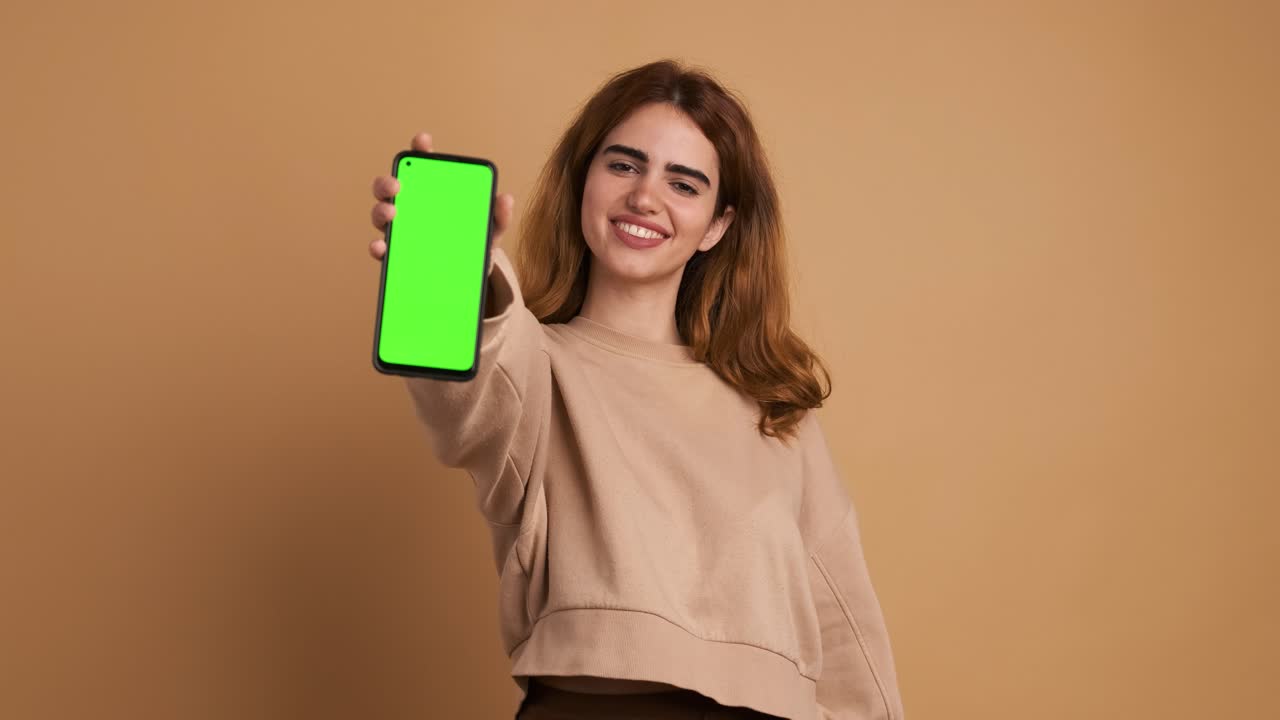 Woman showing cellphone with green screen in studio