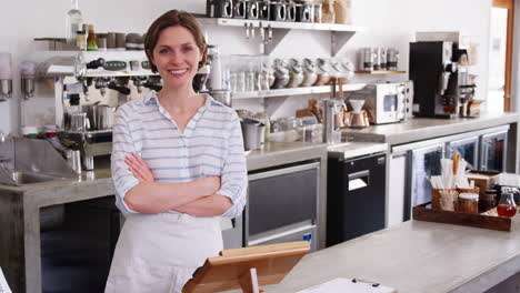 young woman behind counter at a coffee shop smiles to camera