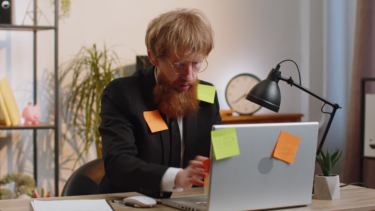 Tired sad exhausted businessman working on laptop at office with many sticker tasks panic attack