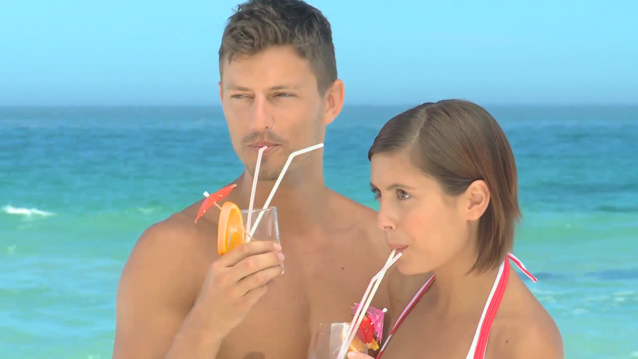 una pareja bebiendo cócteles en una playa.