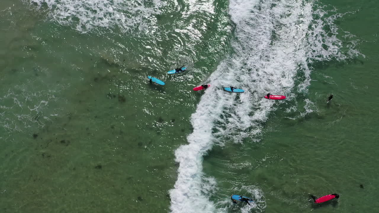 공중 촬영: 교사가 서핑반 학생을 작은 파도 위로 밀어넣고 다른 사람들은 이를 놓침