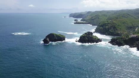 aerial view of coral island with overgrown by trees in ocean,hit by waves during sunny day - timang island, yogyakarta, indonesia