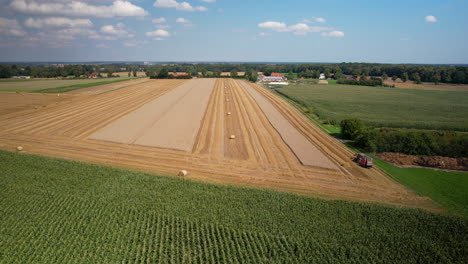 Ländliche-Luftatmosphäre,-Gemähtes-Feld-Mit-Traktor,-Strohballenpressen,-Weitwinkelaufnahme-Von-Bebauten-Feldern,-Erntezeit-In-Polen