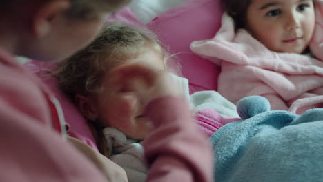 mother caring for sick children lying in bed with flu measuring temperature using thermometer little girls at home with fever child health care