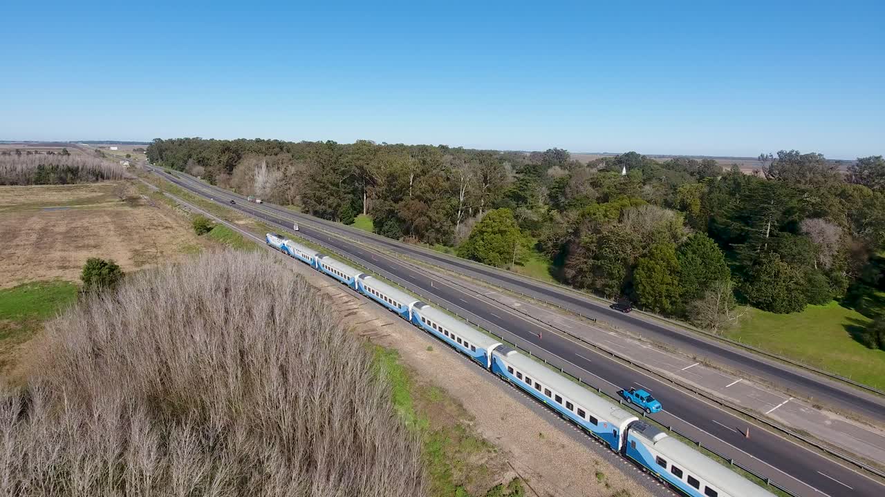 tren de pasajeros azul moviéndose a lo largo de las vías al lado de una autopista, paisaje rural en las afueras de buenos aires