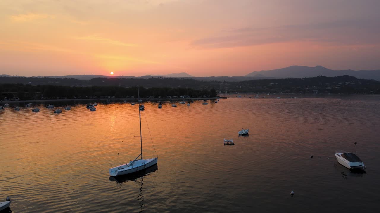 vista aérea de la idílica puesta de sol sobre el lago di garda y la ciudad de sato lombardía italia, frente al lago sereno y reflejo de la luz del sol naranja, disparo de drones