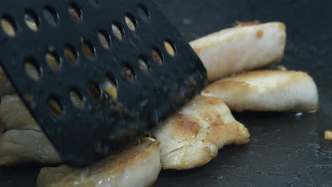 pieces of chicken meat are fried and turned over in a pan with a spatula