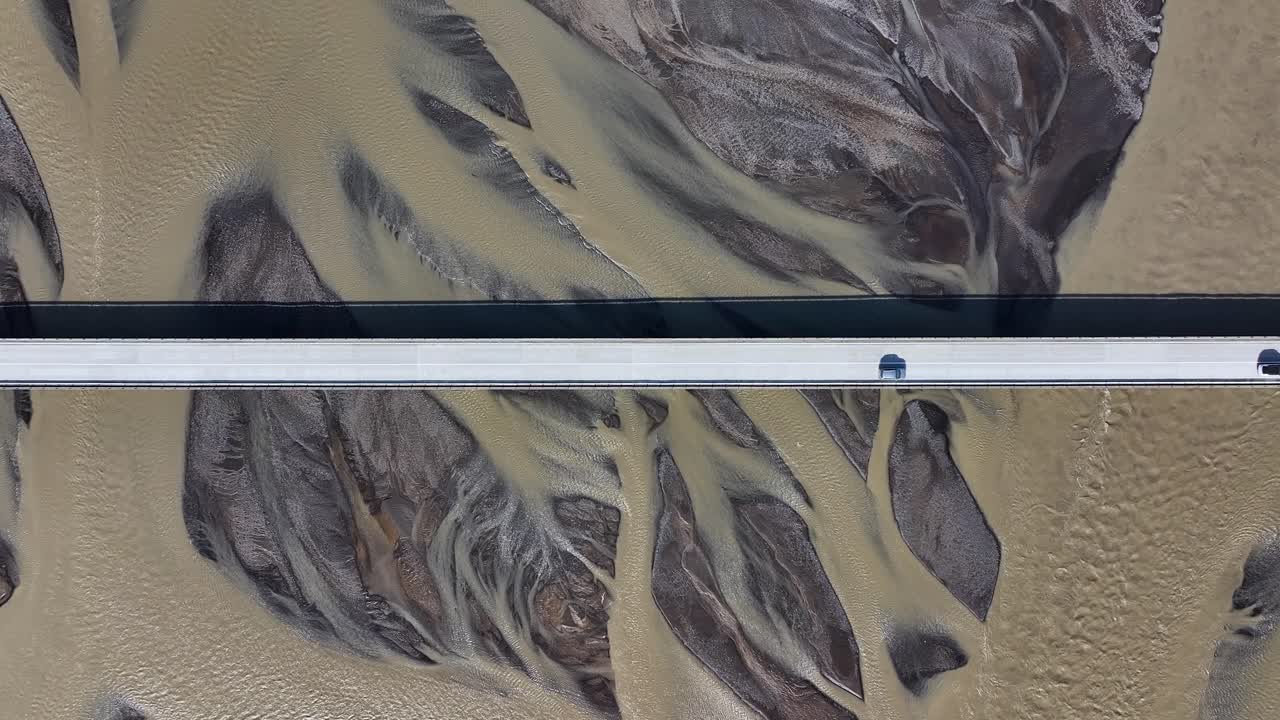 Two vehicles on bridge crossing river delta in Iceland at sunny day. Aerial top down shot. Spectacular pattern of mud and estuary