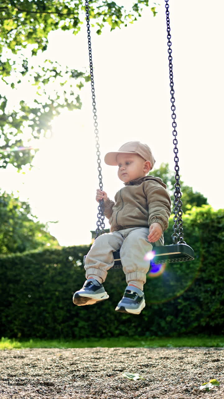 Un bambino siede su un'altalena in un parco cittadino, in un'area giochi. Un bambino piccolo con giacca e scarpe da ginnastica si dondola in un parco giochi all'aperto. Il bambino gioca e si gode il tepore all'aperto. Sviluppo infantile.