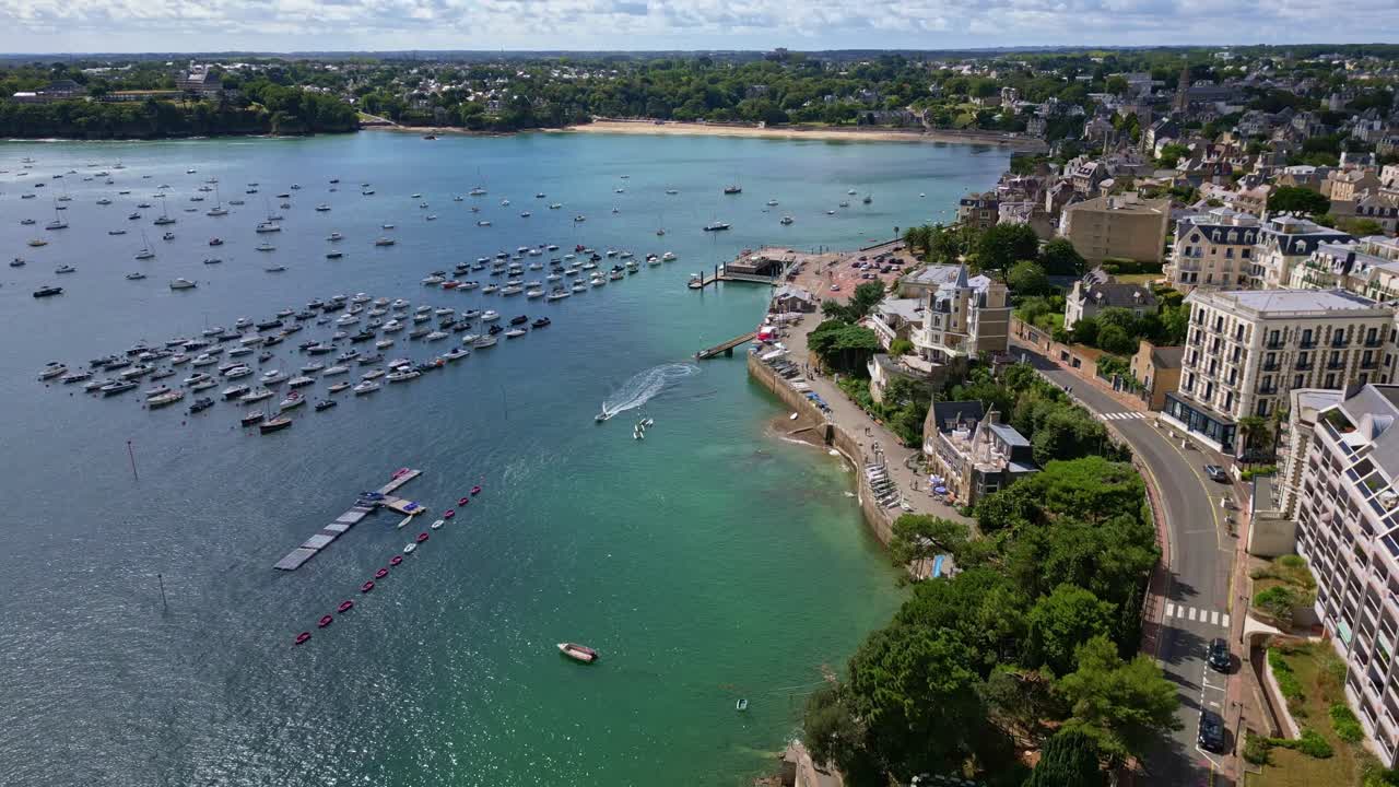 Panoramic aerial view showing the coastal town of Dinard in Brittany, France, with its historic buildings, urban landscape, beautiful coastline, and a rectangular sea pool, drone pulling away