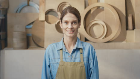 retrato de mujer caucásica en delantal sonriendo a la cámara en taller de carpintería
