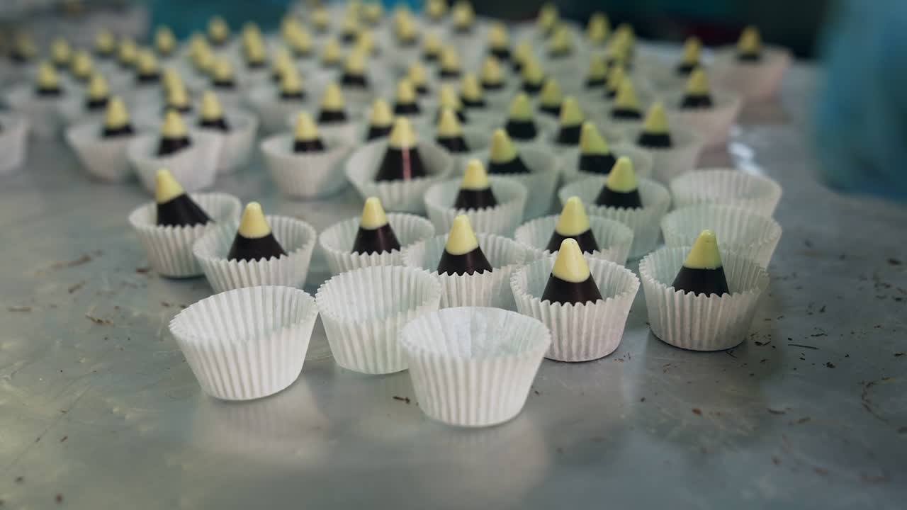 Chocolate cones with white tops are put into individual paper wrapper. Confectionery workers in gloves pack every candy separately. Close up.