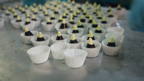 chocolate cones with white tops are put into individual paper wrapper. confectionery workers in gloves pack every candy separately. close up.