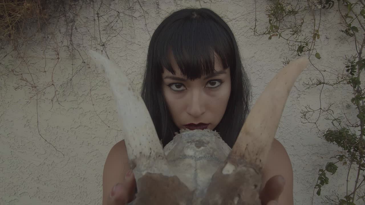 Pull-out of piercing eyes of young woman holding a horned animal skull in her hands.