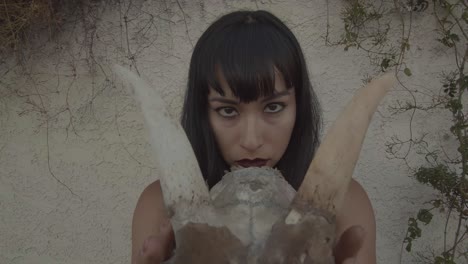 pull-out of piercing eyes of young woman holding a horned animal skull in her hands.