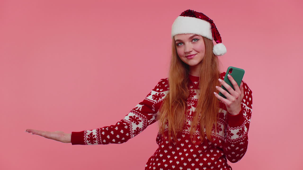 chica en navidad suéter de santa con teléfono móvil mostrando señalando lugar vacío, área de publicidad