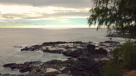 4k hawaii kauai slow pan left to right of backlit ocean waves swirling in small cove and crashing against rocky shoreline with mostly cloudy sky