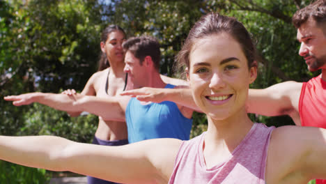 mujer caucásica sonriente practicando yoga con un grupo diverso e instructora femenina en el parque soleado