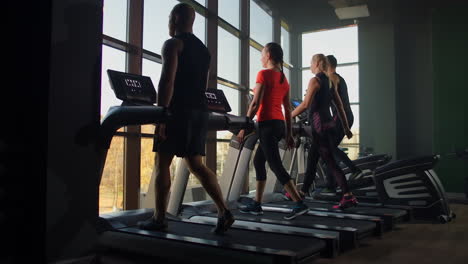 four people young men and women walking on treadmills conducting warm-up before training.