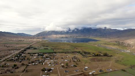 Pedestal-drone-flight-over-the-town-of-Tafi-del-Valle-with-view-on-the-epic-lake-and-the-cloudy-mountain,-slowmo-and-copy-space