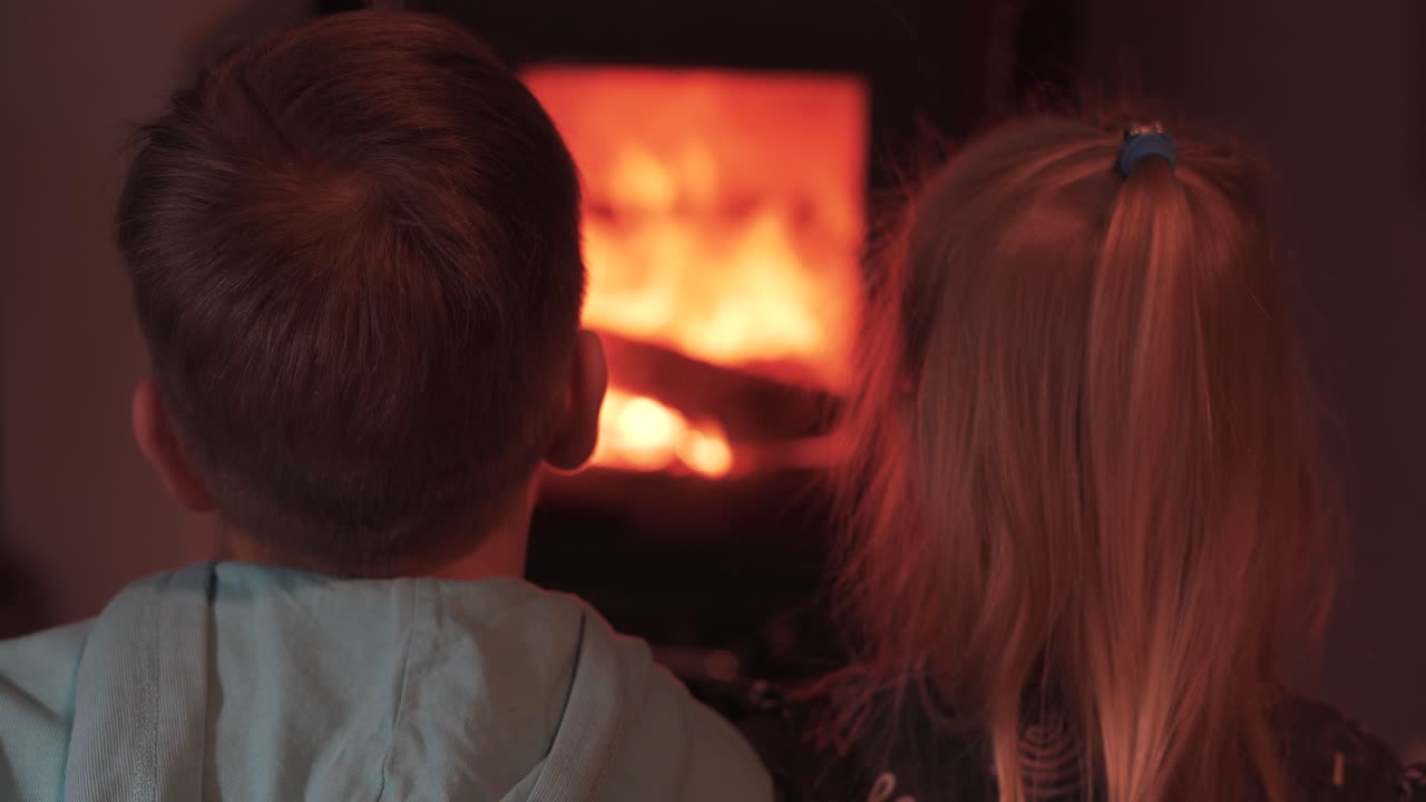Two Happy Little Children Brother and Sister Sitting by the Fireplace and Watching the Fire. Enjoying a Warm Atmosphere and Flame Move. Concept of Happy Family. Static Shot