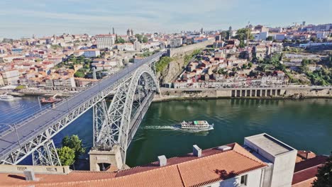 scenic view of porto and vila nova de gaia with boat under dom luís i bridge in bright daylight