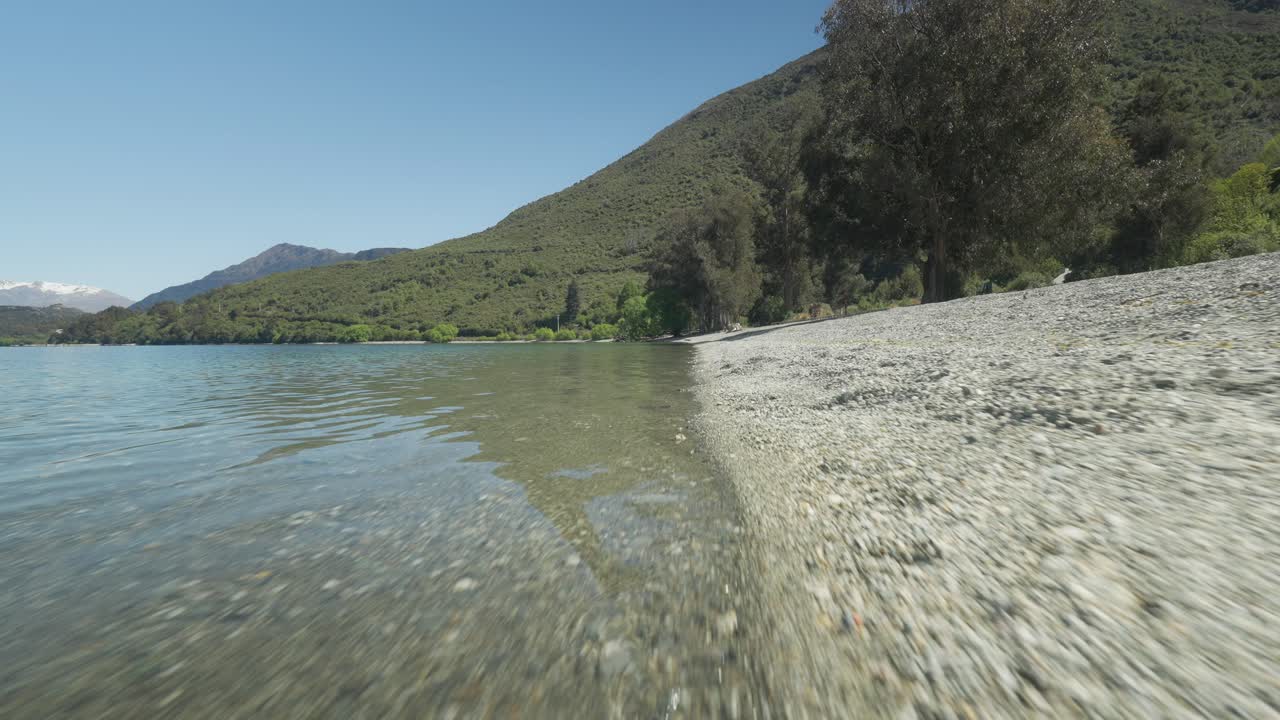 playa de guijarros de la bahía de wilson con aguas tranquilas y frescas del lago wakatipu, ángulo bajo
