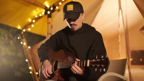 man plays the guitar and sings songs in a tent with light bulbs