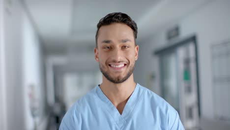 Portrait-of-happy-biracial-male-doctor-wearing-scrubs,-smiling,-slow-motion