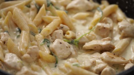 anonymous cook stirring pasta in frying pan with spatula