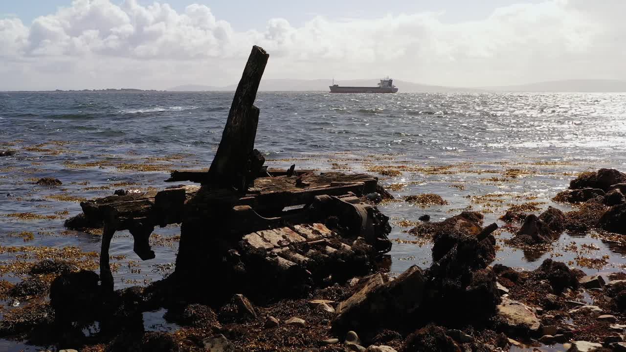 Old broken wooden metal piece of garbage floats on Mutton Island’s rocky shore with the vast ocean and distant boats in Galway Bay, Ireland