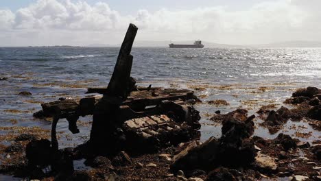 old broken wooden metal piece of garbage floats on mutton island’s rocky shore with the vast ocean and distant boats in galway bay, ireland