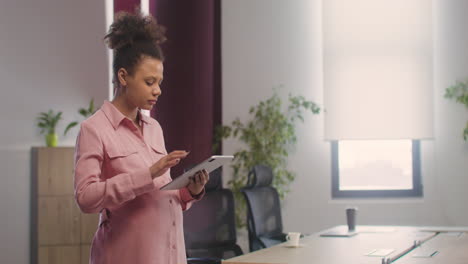 pregnant woman standing in the office while using a tablet