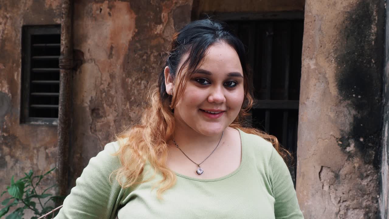 Beautiful young smiling girl posing in front of camera in green blank t-shirt.Close up head shot pretty young woman smile look at camera pose alone outdoor. Professional occupation person.