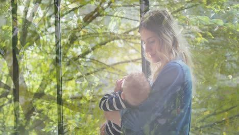 animation of trees over happy caucasian mother holding her baby