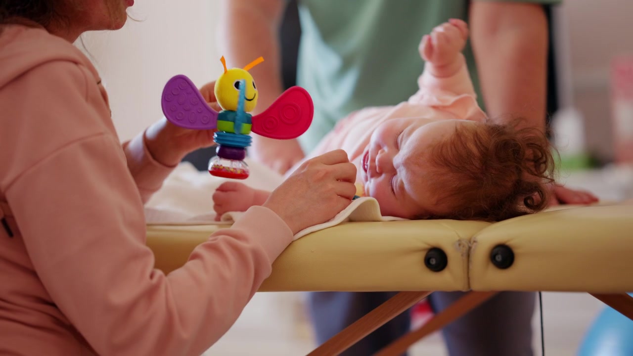 Um bebê descansa confortavelmente durante uma sessão de terapia pediátrica, enquanto os cuidadores utilizam brinquedos sensoriais coloridos para estimular o engajamento e o desenvolvimento.