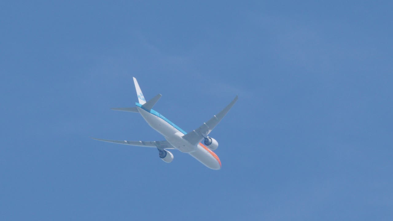Commercial airplane banking mid-flight against clear blue sky, captured from below with steady camera