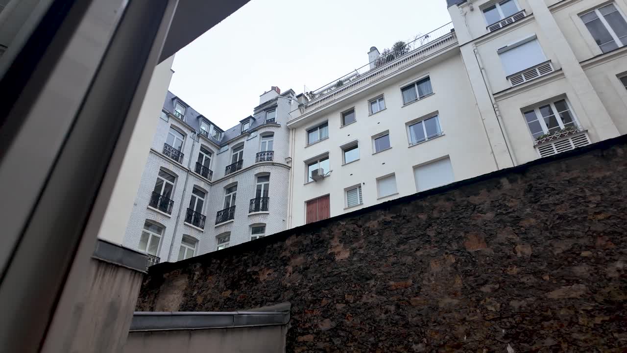 Vista di edifici parigini da una finestra con muro in pietra in primo piano, che mostra architettura classica e paesaggio urbano a Parigi, Francia