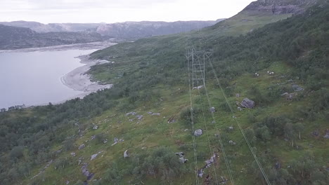 aerial view of power lines along a river on a cloudy day in norway, tracking shot