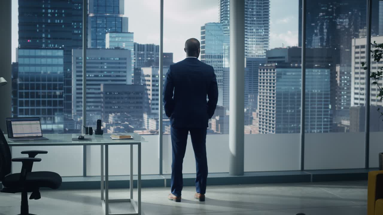 hombre de negocios negro pensativo en un traje a medida de pie en la oficina mirando por la ventana a la gran ciudad. exitoso ejecutivo corporativo pensando estrategia de inversión para la puesta en marcha de comercio electrónico. vista posterior