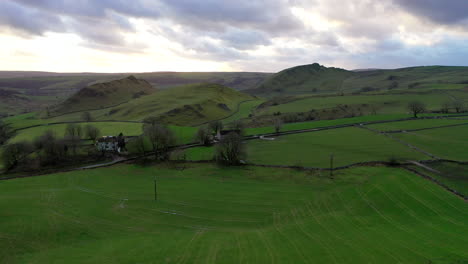 aerial wide shot rising over green fields and hills in the peak district during cloudy sunset