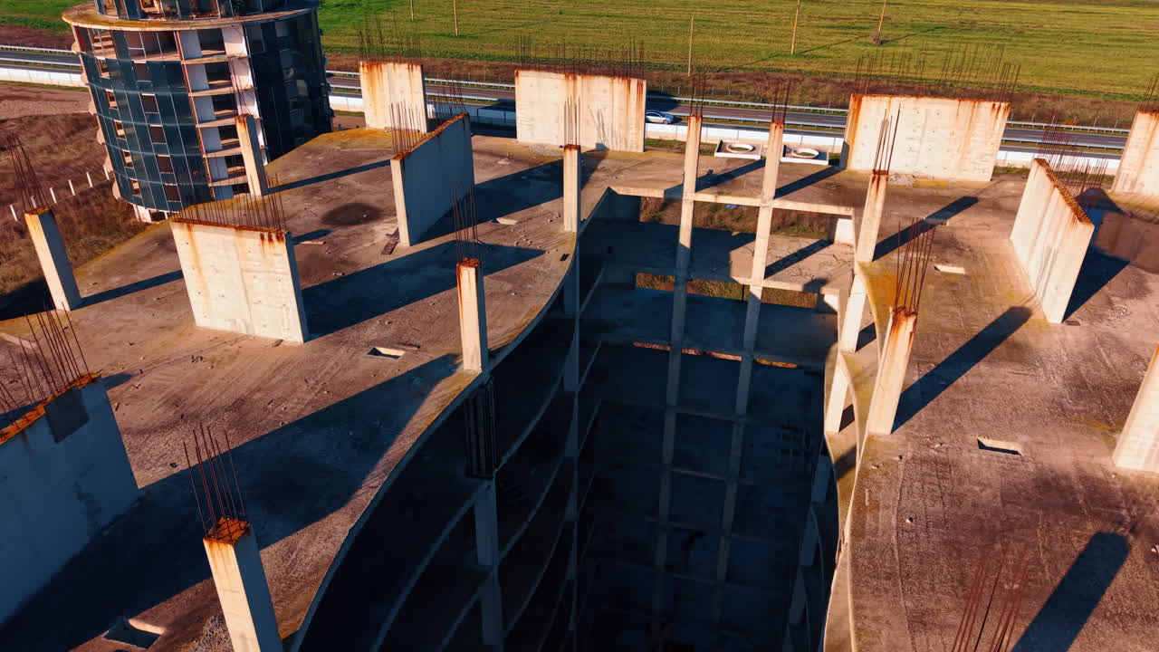 Vlucht over het karkas van de bouw van een gebouw met meerdere verdiepingen. Snelweg met rijdende auto's op de achtergrond